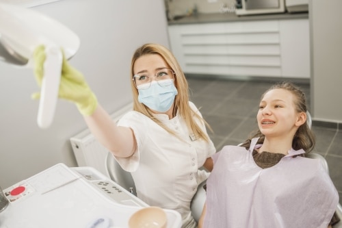 orthodontist checking teeth of girl with braces